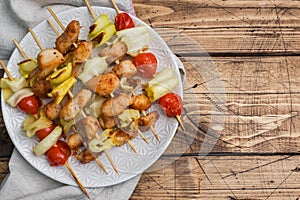 Kebab chicken, zucchini and tomatoes on skewers in a plate. Wooden table. Copy space