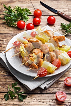 Kebab chicken, zucchini and tomatoes on skewers in a plate. Wooden table