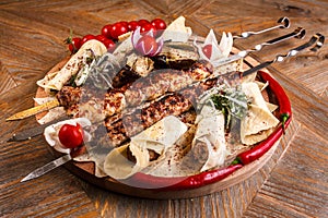 Kebab on skewers on a wooden tray with cherry tomatoes and hot pepper