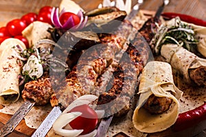 Kebab on skewers on a wooden tray with cherry tomatoes and hot pepper