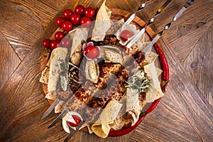 Kebab on skewers on a wooden tray with cherry tomatoes and hot pepper