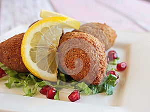 KEBBAH, kibbeh, kibbe or kubbeh with lemon slice and pomegranate seeds closeup served in dish isolated on table side view of photo