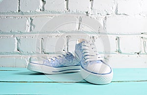 Keds with white laces close-up on wooden flloor against a white brick wall.