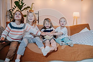 Keen children sitting on a couch, keen on watching television, eating popcorn