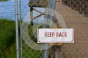 A keep back sign on a chain-link fence