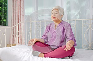 Keep calm and breath. Senior woman meditating in lotus position on bed at home, Healthy morning routine and meditation concept