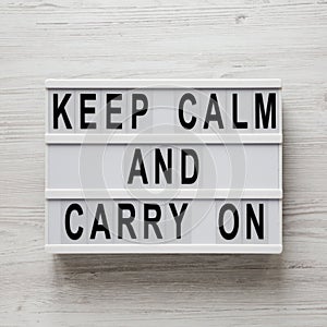 `Keep calm and carry on` words on a lightbox on a white wooden surface, top view. Overhead, from above, flat lay