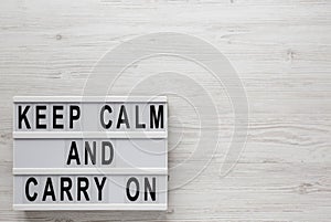 `Keep calm and carry on` words on a lightbox on a white wooden surface, top view. Overhead, from above, flat lay. Copy space