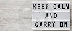 `Keep calm and carry on` words on a modern board on a white wooden background, top view. Overhead, from above, flat lay. Copy