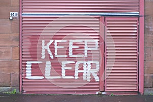 Keep clear sign on red roller shutter door large white spray paint text