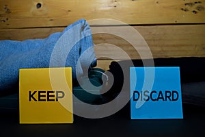 Keep and Discard write on a sticky note between fashion clothes folded and stack isolated on wooden background