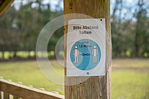 Keep distance of 1,5 meters german Corona Covid-19 Rule Sign on a tree trunk at a amusement park safari park