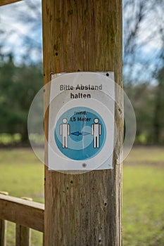 Keep distance of 1,5 meters german Corona Covid-19 Rule Sign on a tree trunk at a amusement park safari park, vertical shot