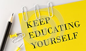 Keep Educating Yourself word on the yellow paper with office tools on white background