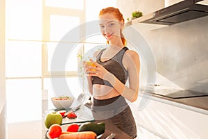 Athletic young red haired woman in the kitchen with a glass of fruit centrifuged juice photo