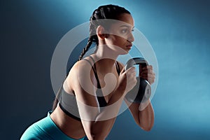 Keep going so you can keep improving. Studio shot of a sporty young woman doing kettlebell squats against a blue