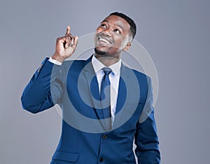 Keep looking up. Cropped shot of a handsome young businessman pointing upwards in studio against a grey background.