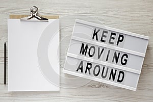 `Keep moving around` words on lightbox, noticepad and pencil on a white wooden background, top view. From above, flat lay,