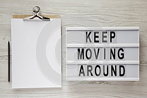 `Keep moving around` words on modern board, noticepad and pencil on a white wooden background, top view. From above, flat lay,