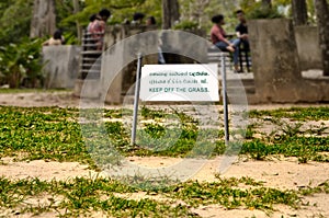 Keep off the grass sign in tropical park with poor bad lawn