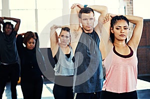 Keep this position for a bit. a focused group of young people standing in a row and stretching while one looks into the