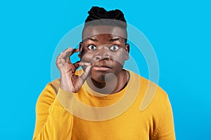 Keep Quiet. Young Black Man Making Zipping Mouth Gesture Over Blue Background