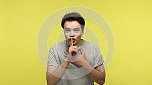 Keep in secret. Young man showing silence gesture with finger, asking be silent