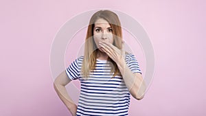 Keep silence. Scared woman covering mouth with hands while posing to camera on pink studio background. Shocked girl close lips