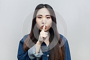 Keep silence. Serious strict bossy brunette woman looking at camera, keeps finger near lips.