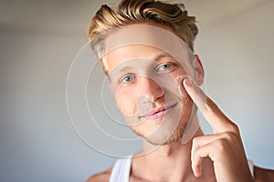 Keep the skin moisturized and protected. a young man applying moisturizer to his face.