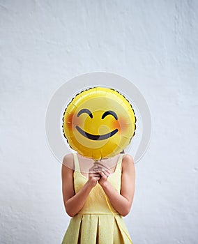 Keep smiling. Studio shot of an unrecognizable woman holding a smiling emoticon balloon in front of her face against a