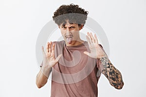 Keep this thing away from me. Stylish tattooed man expressing disgust and aversion raising palms to protect himself from