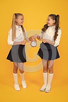 Keep your students safe and on time. Happy little girls holding retro clock during school time on yellow background