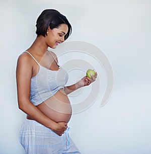 Keep yourself healthy, keep baby healthy. Studio shot of an attractive young pregnant woman holding a green apple.