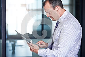 Keeping abreast of the latest in business news. a well dressed businessman using a tablet while standing in the office.