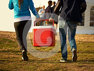 Keeping it cool. Rear view of two people carrying a cooler box down to the stage at a music festival.