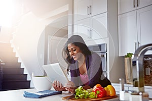 Keeping her recipes digitized. a young woman using a digital tablet while preparing a healthy meal at home.