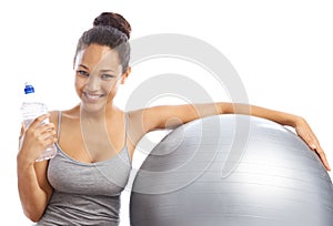 Keeping her water at hand. A young woman sitting next to an exercise ball holding a bottle of water.