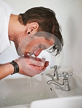 Keeping his complexion clean. a young man washing his face in a bathroom sink.