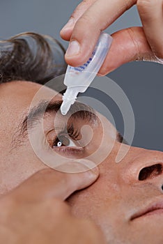 Keeping his eyes clear. Studio shot of a young man putting drops into his eye.