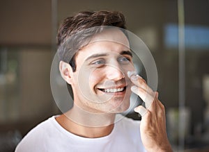 Keeping his face looking fresh and relaxed. Closeup of a young man applying lotion to his face.