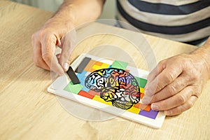 Keeping mind active elderly male hand manipulates colorful wooden puzzle, brain health and mental well-being, cognitive training,