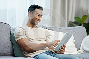 Keeping myself entertained during the weekend. a handsome young man sitting alone in his living room and using a digital