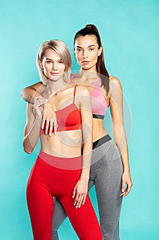 Keeping their body fit. Two young and beautiful sporty girls in sportswear looking at camera while standing against blue