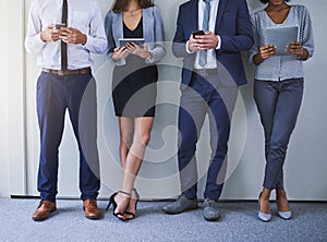 Keeping up with the pace of business. a group of unrecognizable businesspeople using wireless technology while standing