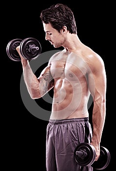 Keeping well-toned. Side view of a bare-chested young man lifting dumbbells isolated on black.