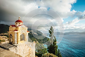 Kefalonia, Ionian islands, Greece. Colorful Proskinitari shrine lantern on pedestal. Coastline with cloudscape above in