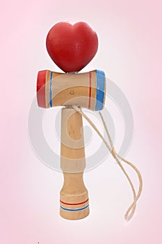 Kendama, a traditional Japanese toy consisting of a sword and a ball connected by a string rolled in heart shape, on pink