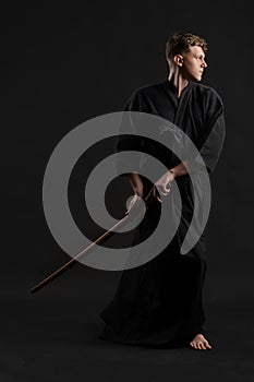 Kendo guru wearing in a traditional japanese kimono is practicing martial art with the shinai bamboo sword against a