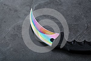 Kerambit dagger with a rainbow-colored blade on a dark textured background.